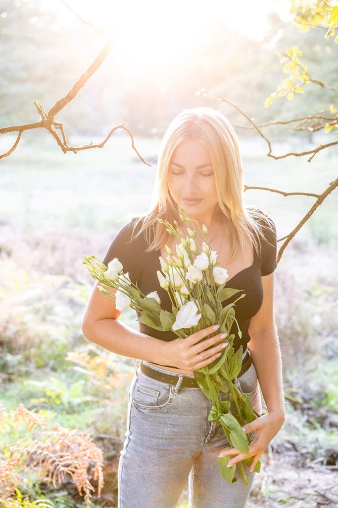 Sommerporträt NRW – Frau mit Blumenstrauß blickt nach unten im Sonnenlicht