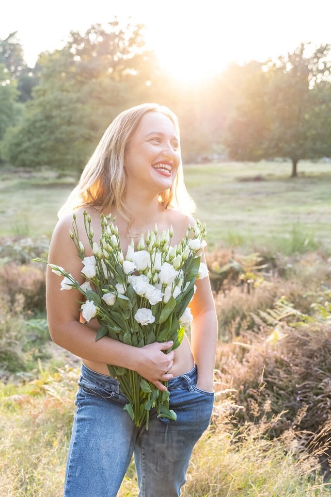 Outdoor Lächeln NRW – Lachende Frau mit Blumenstrauß im warmen Sonnenlicht