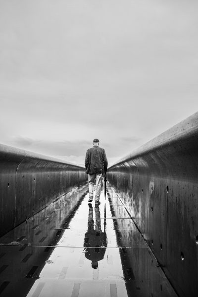 Mann mit Regenschirm geht über nasse Brücke – Schwarzweiß Streetfotografie