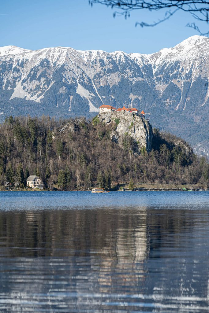 Blick auf eine Burg auf einem Felsen über dem Bled See mit verschneiten Bergen