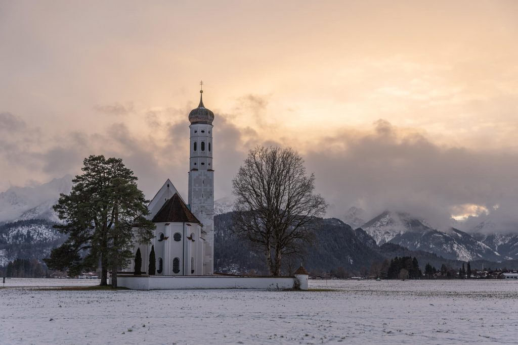 Kirche im winterlichen Schneefeld vor leuchtendem Sonnenuntergang