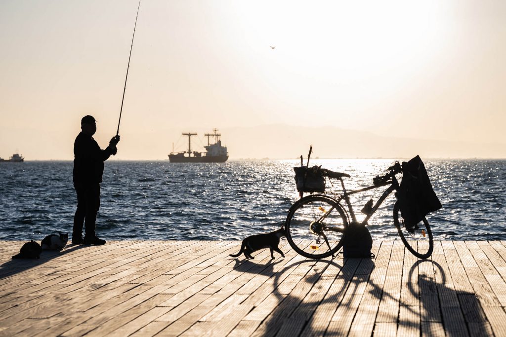 Ein Mann angelt am Meer, daneben ein Fahrrad, im Sonnenuntergang