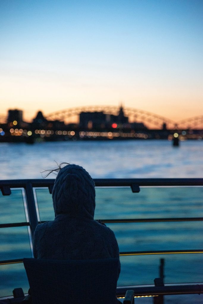 Person mit Kapuze blickt über den Rhein bei Sonnenuntergang in Köln.