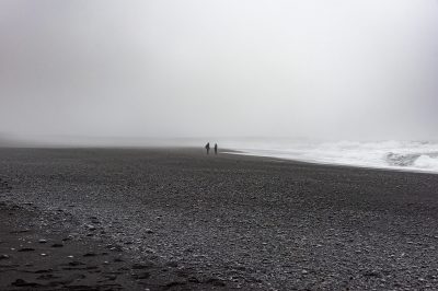 Zwei Menschen spazieren am dunklen Strand im Nebel – Islandfotografie