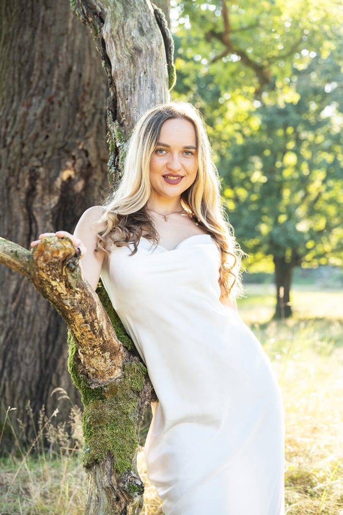 Outdoorporträt mit Baumstamm Köln – Frau in weißem Kleid lehnt an moosbewachsenem Stamm