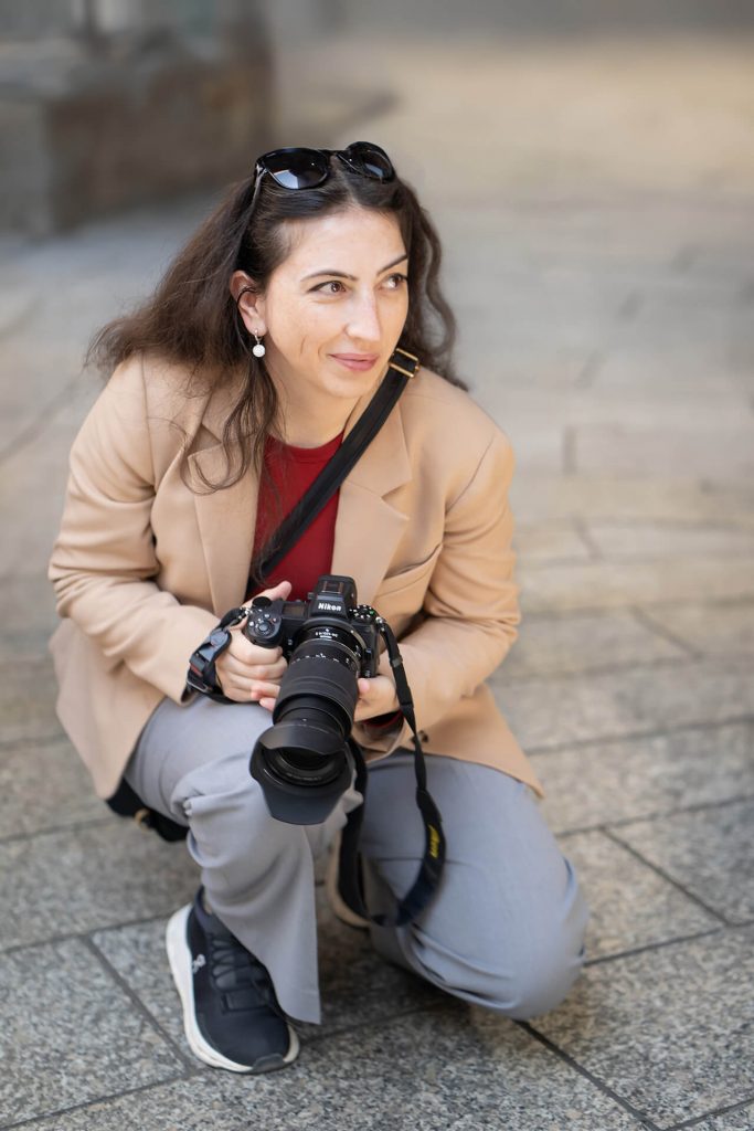 Porträt von Julia Tschirka – Fotografin kniet mit Nikon-Kamera in der Kölner Innenstadt