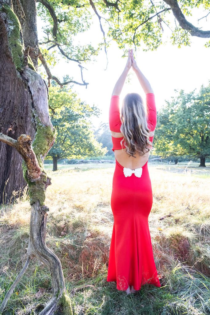 Yoga-inspiriertes Porträt Köln – Rückansicht einer Frau im roten Kleid unter Bäumen vor der Sonne