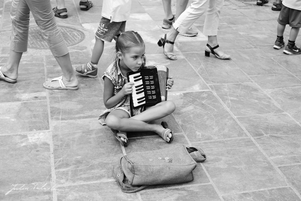 Mädchen spielt Akkordeon auf dem Boden – Streetfotografie in Schwarzweiß