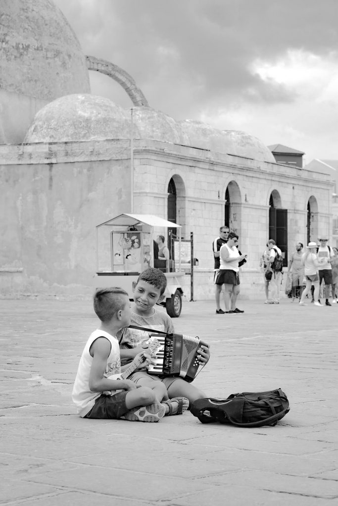 Zwei Jungen musizieren auf Platz mit Akkordeon und Ukulele – Schwarzweißaufnahme