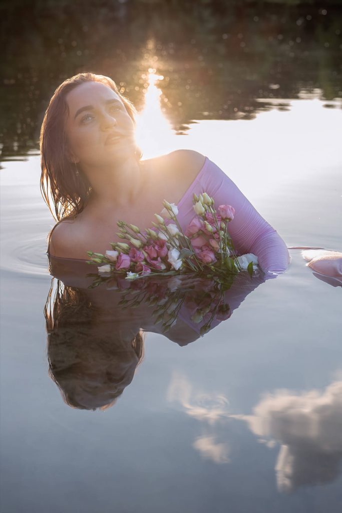 Frau mit Blumen im Wasser, Sonne reflektiert hinter ihr