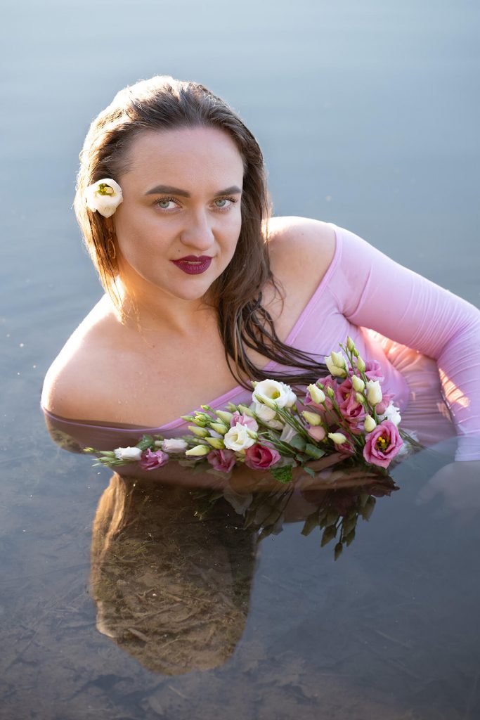 Frau mit weißer Blume im Haar, im Wasser liegend mit Blumenbouquet