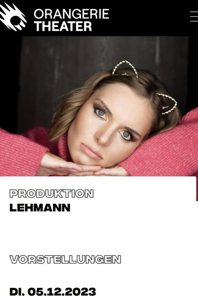 Schauspielerin Carolin Lehmann in pinkem Rollkragenpullover mit ernster Miene, goldenen Katzenohren und Ringlicht im Hintergrund.