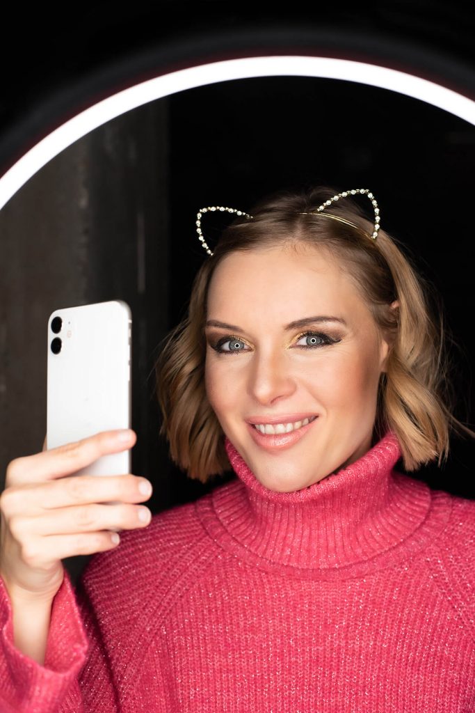 Schauspielerin Carolin Lehmann lächelt freundlich in die Kamera, trägt einen pinken Rollkragenpullover und goldene Katzenohren.