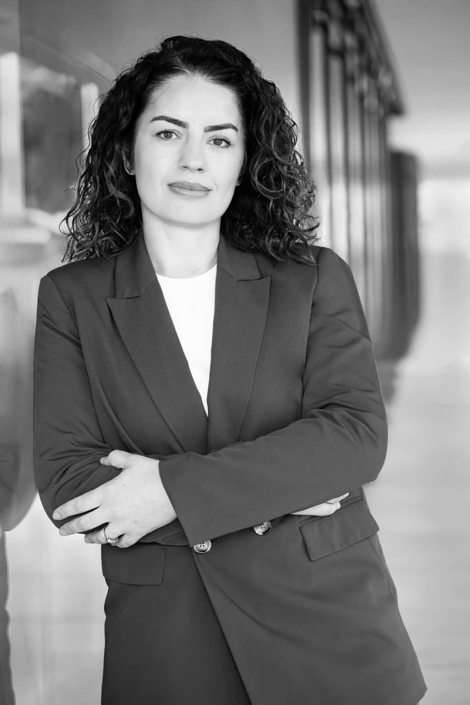 Klassisches Schwarzweiß-Bewerbungsfoto einer Frau im Business-Look vor moderner Architektur.