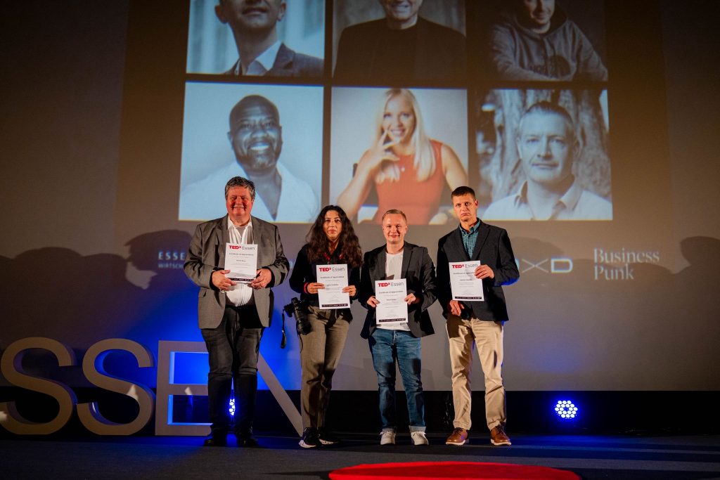 Gruppenfoto bei TEDxEssen 2025 mit mehreren Personen, die Zertifikate auf der Bühne halten.
