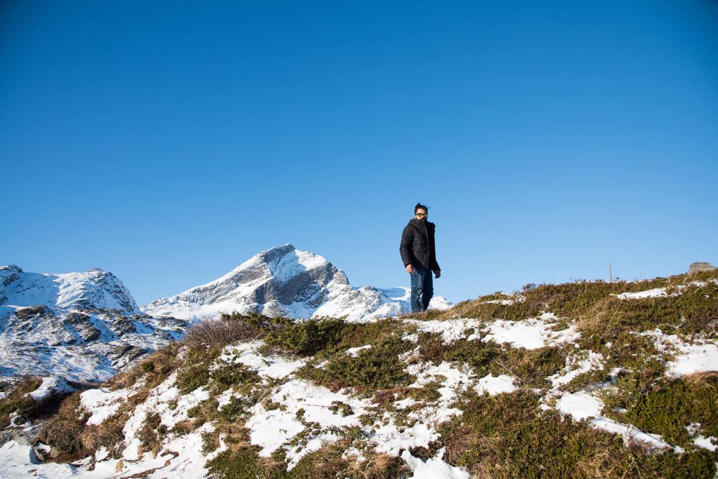 Person steht auf einem Hügel vor klarer, winterlicher Bergkulisse.