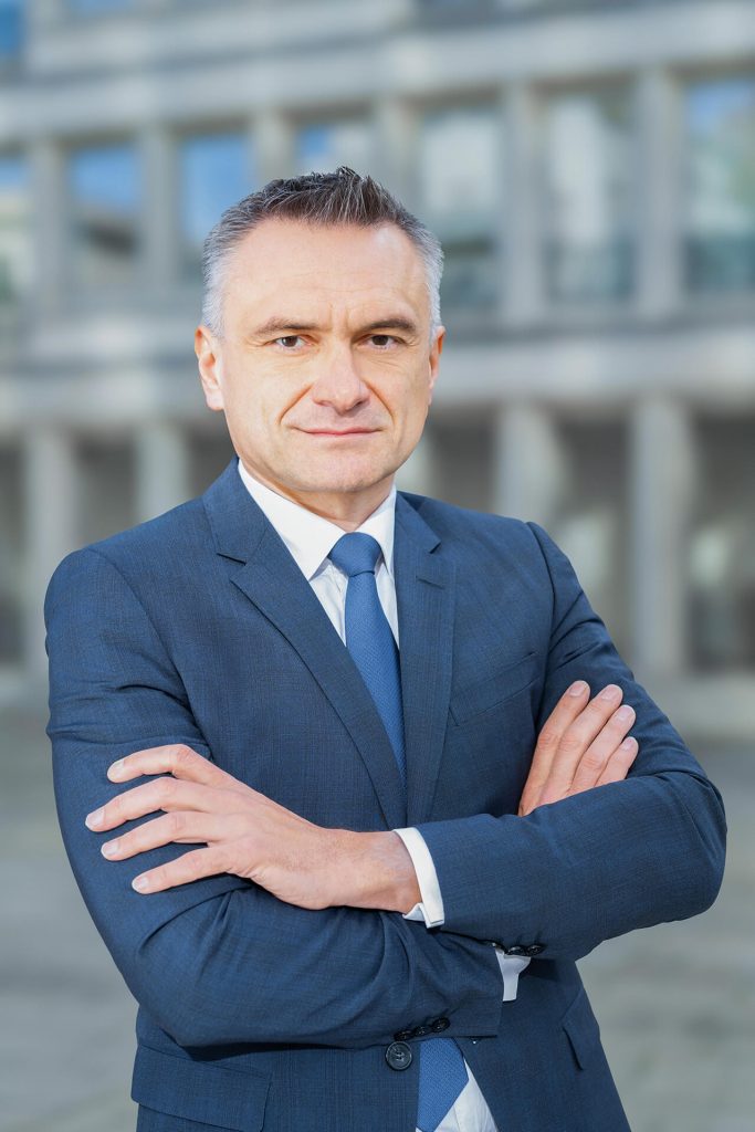 Porträt eines Geschäftsmanns im blauen Anzug mit verschränkten Armen vor modernem Gebäude