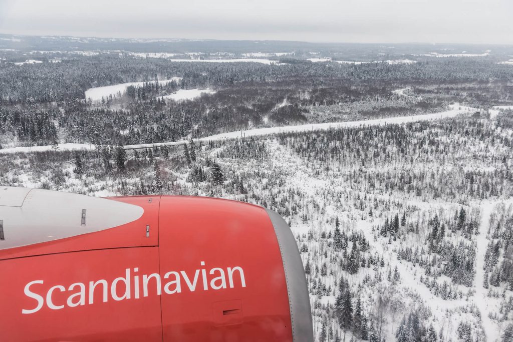 Flugzeugflügel mit roter Motorverkleidung im Anflug über verschneite Wälder.