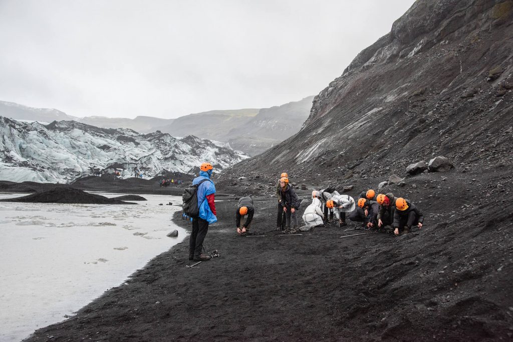 Menschen rüsten sich für eine Wanderung in rauer Gletscherlandschaft.