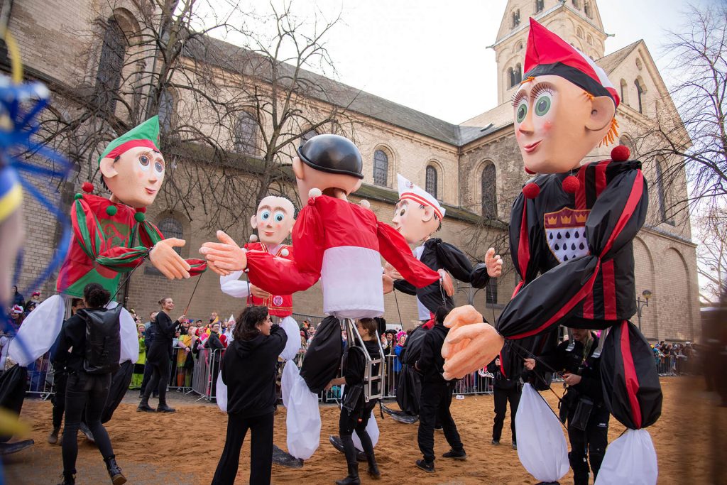 Riesige bunte Figuren tanzen beim Karnevalsumzug in Köln vor Publikum.