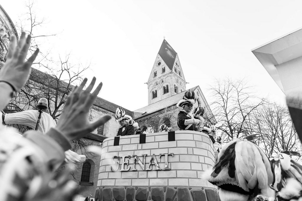 Schwarz-Weiß-Foto des Senat-Wagens im Kölner Karneval mit jubelnden Händen im Vordergrund.