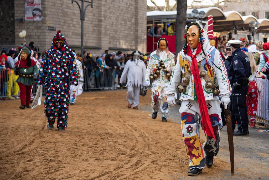 Traditionelle Figuren mit Glocken und bemalten Kostümen beim Kölner Karnevalsumzug.