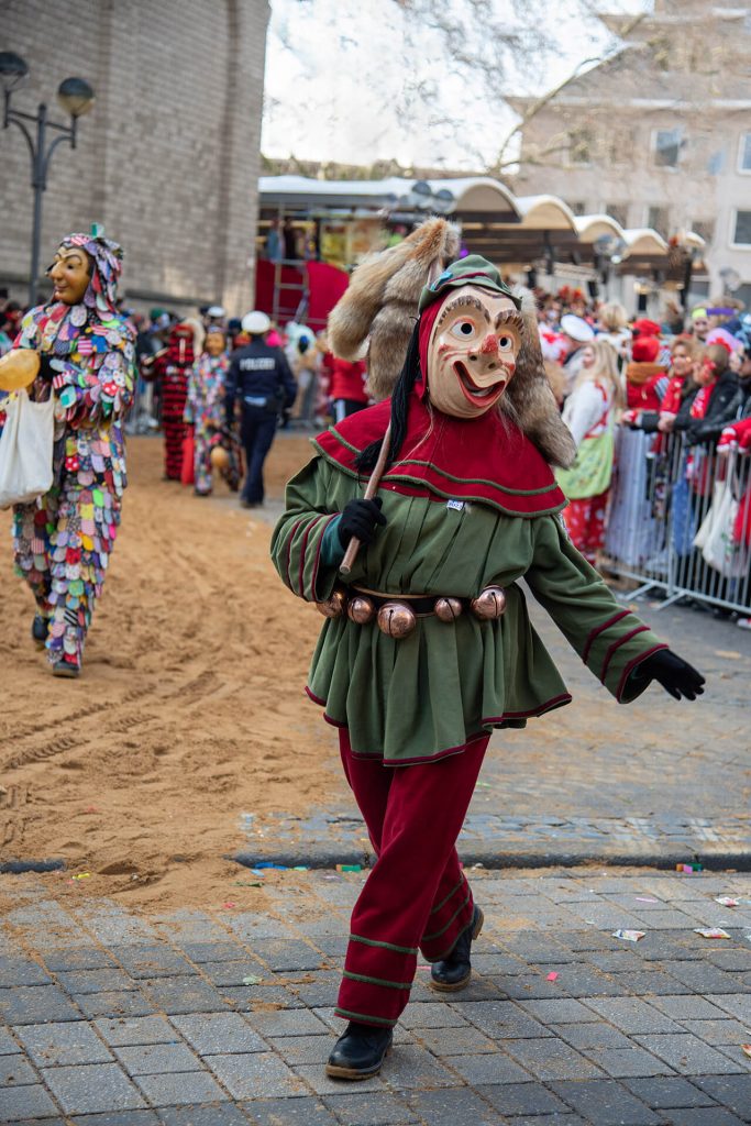 Traditionelle Karnevalsfigur in grün-rotem Kostüm mit Maske, schreitet durch den Kölner Karnevalsumzug.