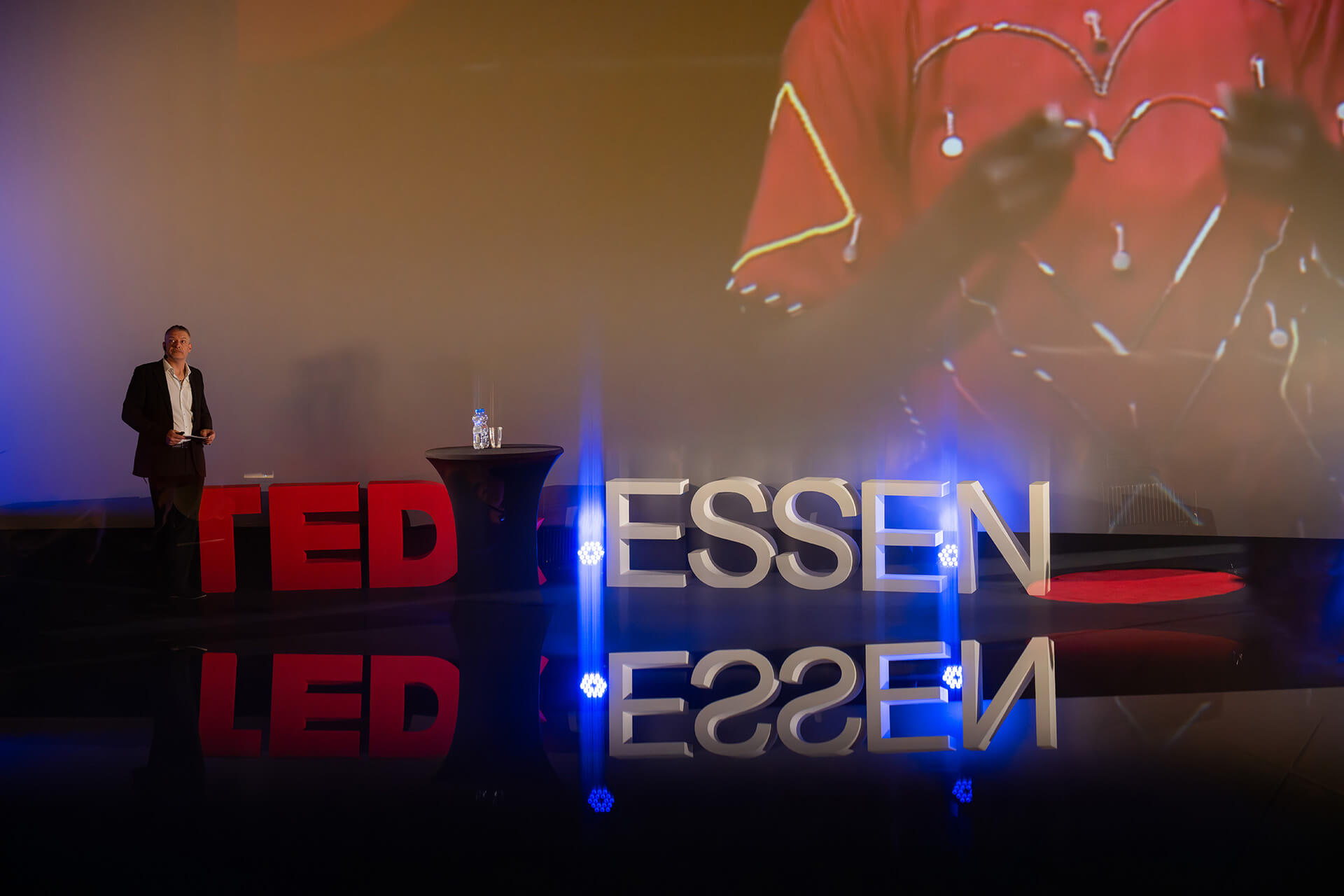 Moderator Dirk Brueckner auf Bühne mit "ESSEN"-Schriftzug bei TEDxEssen