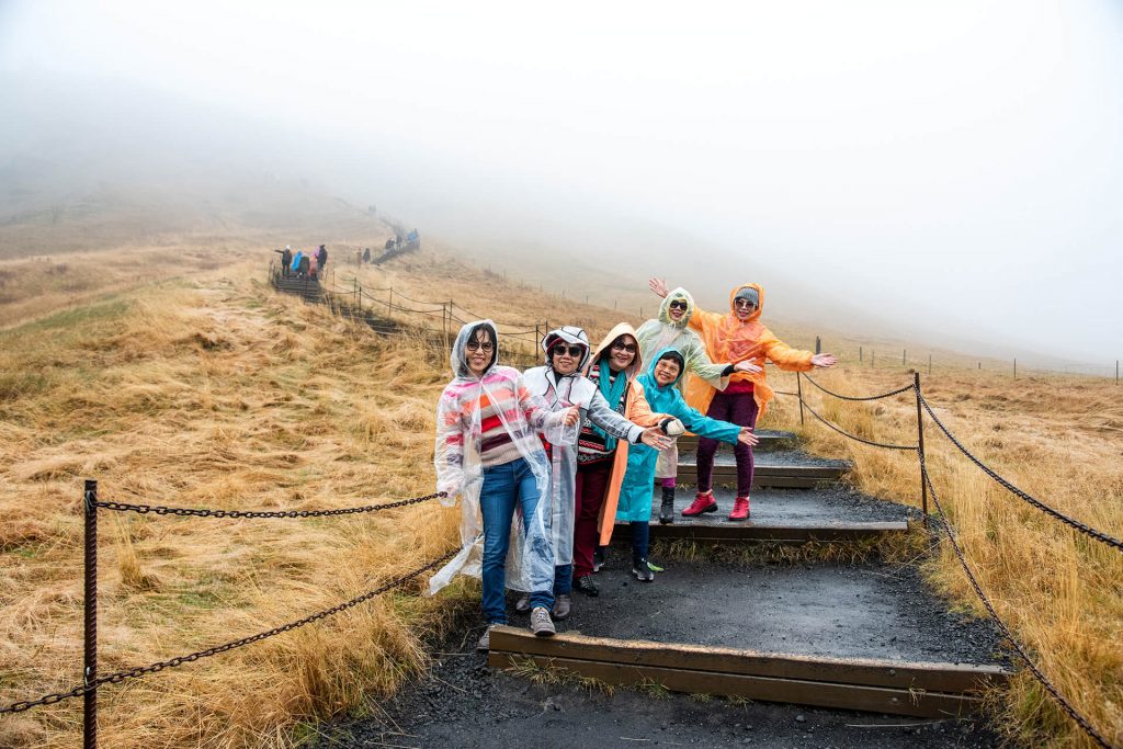 Reisegruppe in bunten Ponchos posiert lachend in nebliger Landschaft.