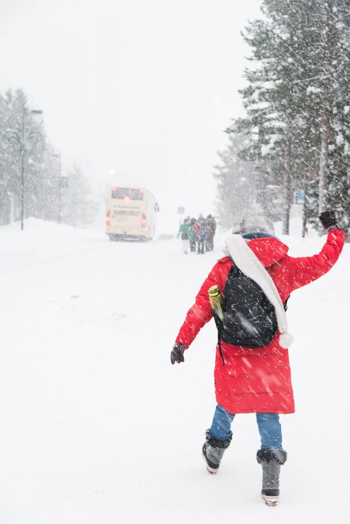 Person im roten Mantel läuft durch starken Schneefall auf einer verschneiten Straße.