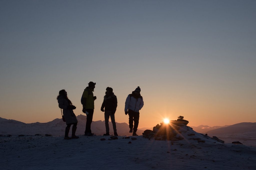 Vier Personen stehen als Silhouette im warmen Sonnenuntergang in einer winterlichen Berglandschaft.