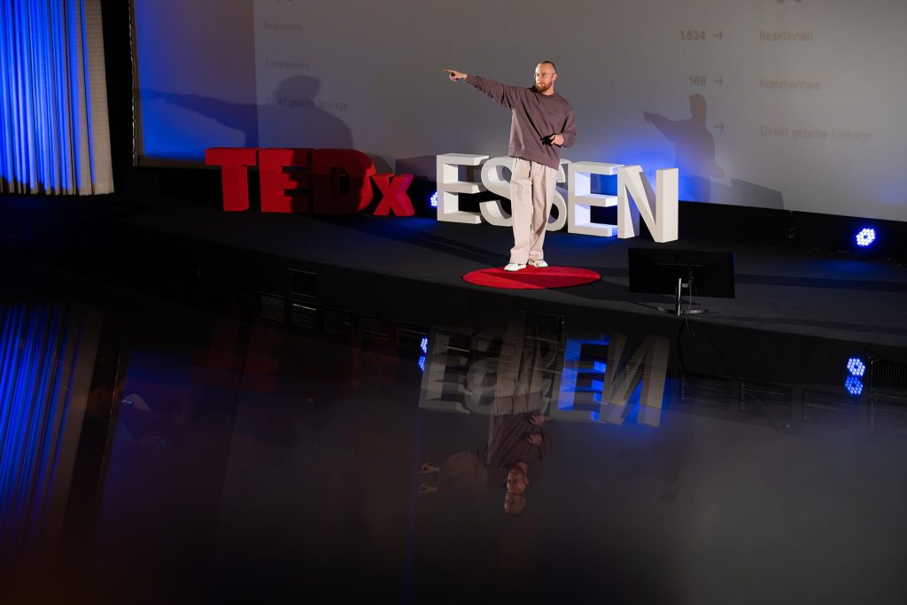 Redner auf der Bühne bei TEDxEssen zeigt mit Geste in die Ferne, Marcel Pesch – Build Your AI Team and Scale Your Business