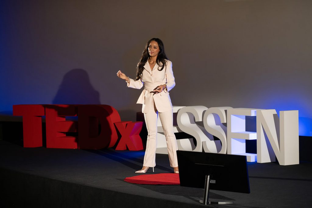 TEDxEssen Rednerin in elegantem Hosenanzug auf der Bühne, Railey Molinario mit der Rede: The Missing Intelligence Behind Love, Leadership and Life