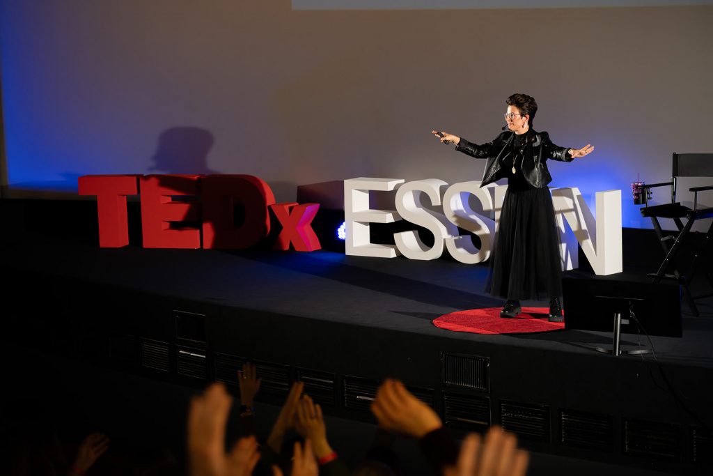 Rednerin im schwarzen Outfit mit ausdrucksvoller Geste bei TEDxEssen, Claudia Gersdorf mit der Rede: Wirkung durch Selbstbestimmung. Der Rebel’s Guide.