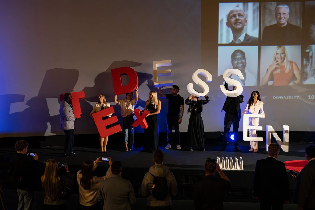 TEDxEssen Redner halten große Buchstaben des Events auf der Bühne hoch