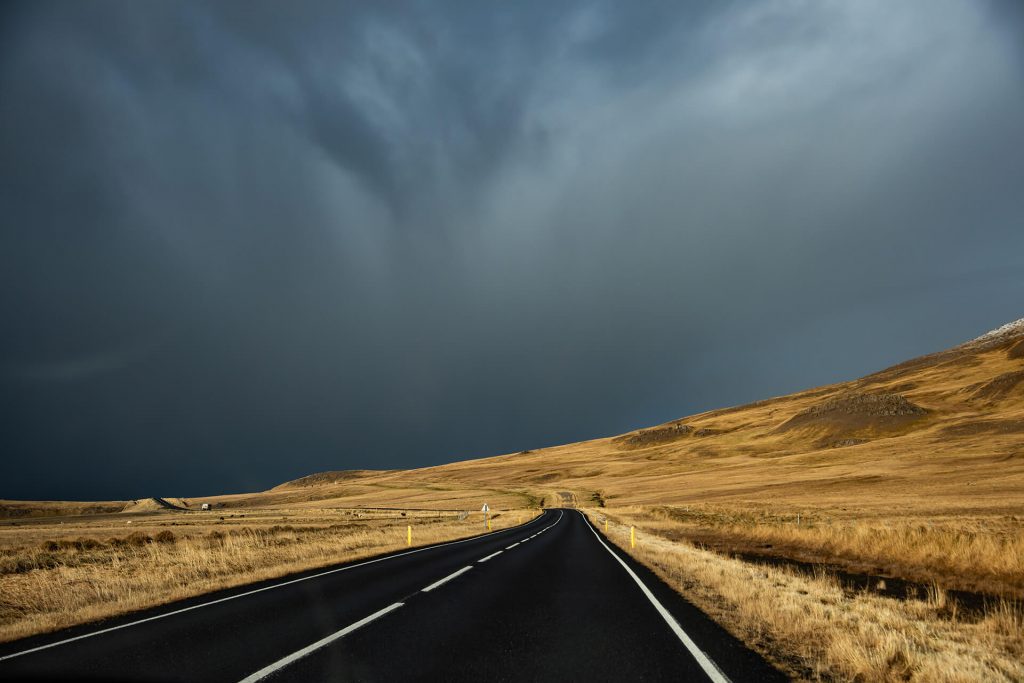 Leere Straße führt in eine dunkle Sturmfront über goldener Landschaft aus Island.