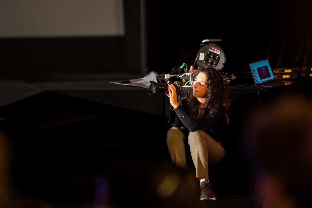 Julia am Bühnenrand und fotografiert mit Nikon Z7II Kamera während des TEDx-Events. die Redner