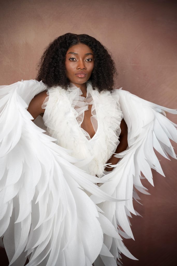 Ganzkörper-Porträt einer Frau mit großem Flügel-Design im weißen Outfit