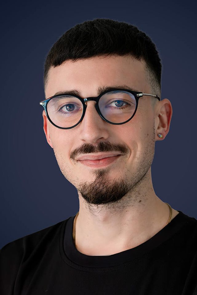 Business Bewerbungsfoto in Köln mit dunkelblauem Hintergrund, junger Mann mit Brille, modern und seriös.