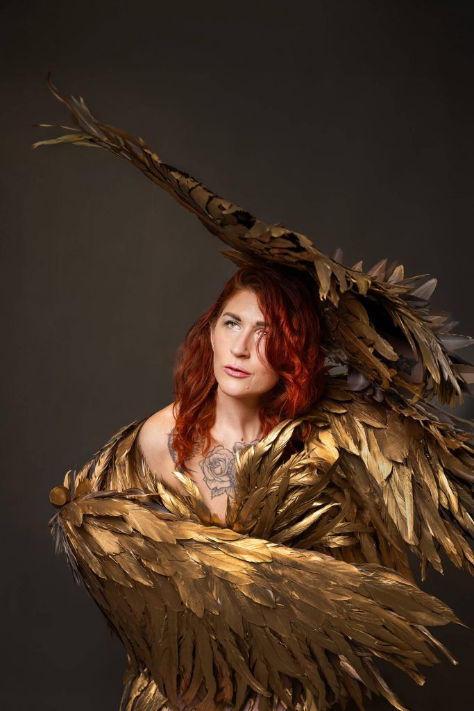 Frau mit roten Haaren in goldenem Federkostüm bei einem Fine Art Portraitshooting in Köln