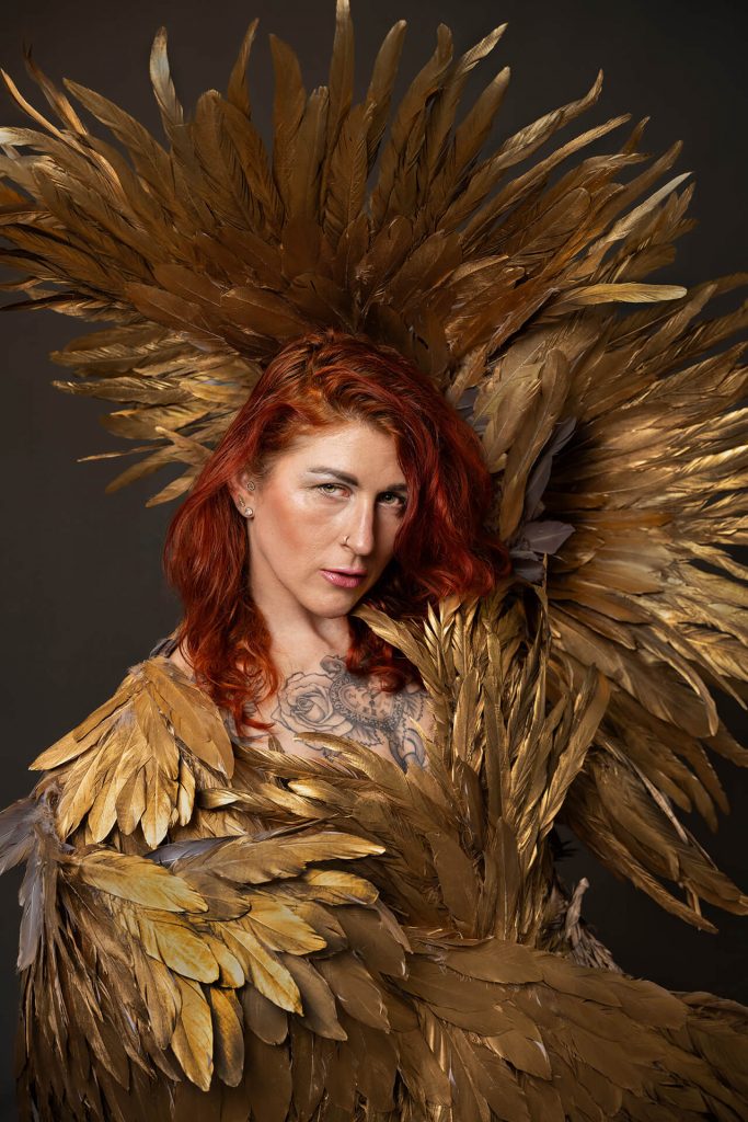 Intensives Portrait einer Frau mit roten Haaren und goldenen Federn im Studio