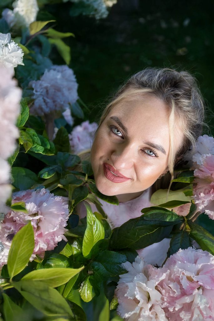Frau zwischen pinken Frühlingsblüten bei einem romantischen Portraitshooting im Grünen